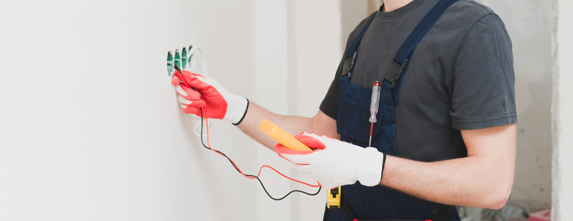 An emergency electrician in Petaluma tests electrical wiring inside a wall using insulated gloves and a voltage meter.