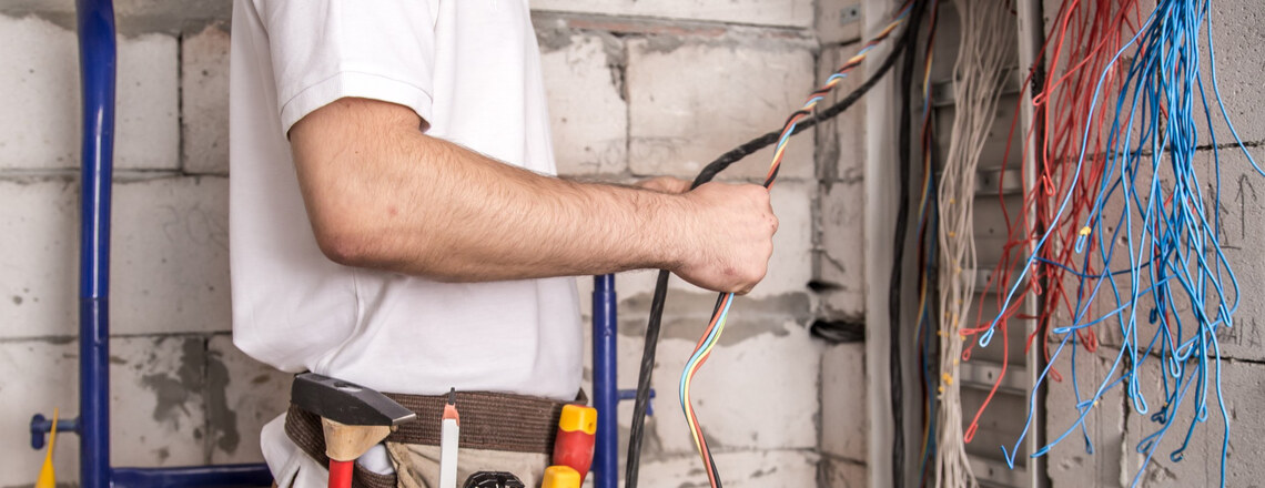 An electrician works with exposed electrical wiring in a residential wall.