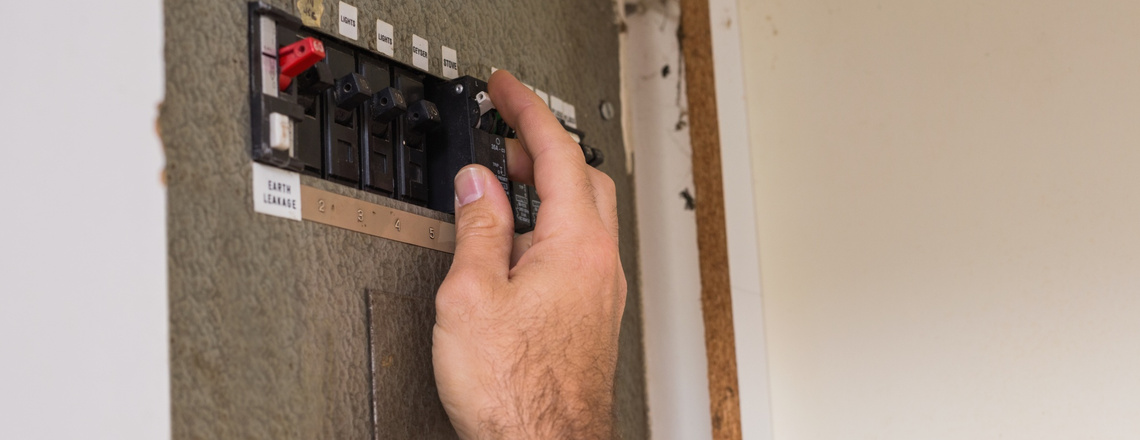 A person adjusts a circuit breaker in an older breaker box, highlighting the need for electrical panel upgrades.